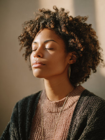 A woman sits quietly, eyes closed, practicing mindfulness and self-care as part of a 7-day plan designed for those in treatment, bathed in soft light.の素材