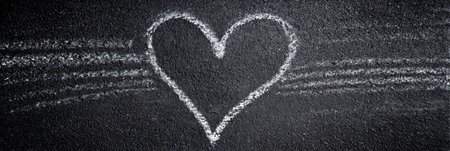 Chalk marks create a heart symbol on a dark textured surface, capturing a moment of artistic expression and emotional connection in a warm environment.の素材
