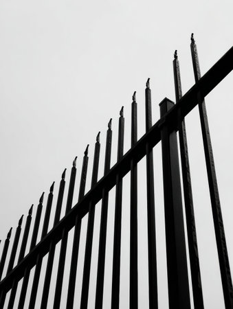 A tall metal fence stretches upward, featuring sharp spikes topped with birds resting quietly against the overcast sky in a city setting.の素材