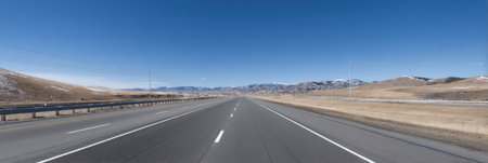 Open highway leads through golden fields toward majestic mountains, with a bright sky above and a sense of tranquility in the surroundings.の素材