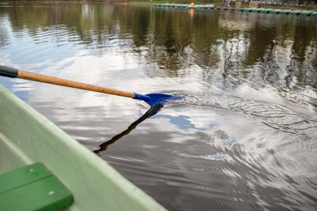 A person rows a small boat on a tranquil lake surrounded by green trees, showing the peaceful nature of early spring.の写真素材