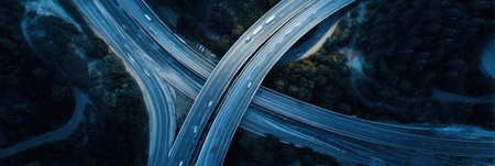 Traffic flows through a complex highway interchange as vehicles navigate the winding roads amid fading daylight. Surrounding trees add a contrast.の素材