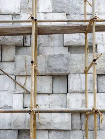 Bamboo scaffolding surrounds a meticulously arranged stone wall under construction, showcasing the blend of nature and craftsmanship in an urban area.の素材