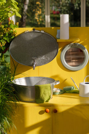 A sunny outdoor workspace showcases bright yellow cabinets with a large metal tub, gardening tools, and vibrant green plants, creating a cheerful atmosphere.の写真素材