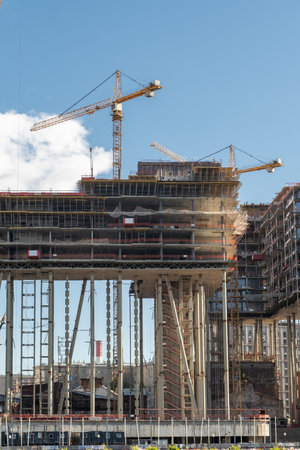 Workers and machinery are busy constructing a high-rise building with cranes operating in the...