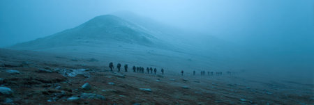 A line of hikers navigate a fog-covered mountain path, surrounded by rocky terrain and low visibility in the early morning light.の素材