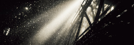 Bright rays penetrate the darkness, revealing a cascade of sparkling particles swirling in the air, creating an enchanting atmosphere in an industrial setting.の素材