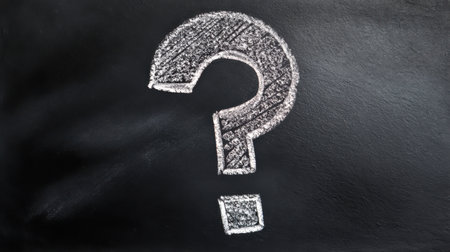 A chalk question mark is drawn on a blackboard, showcasing a textured surface that suggests a classroom or educational environment.の素材