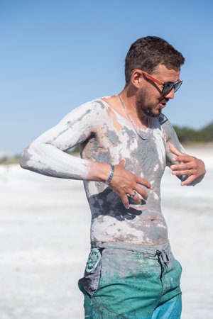 Individual enjoys a unique spa experience by applying therapeutic mud to his body while surrounded by a bright, sunny environment.の写真素材