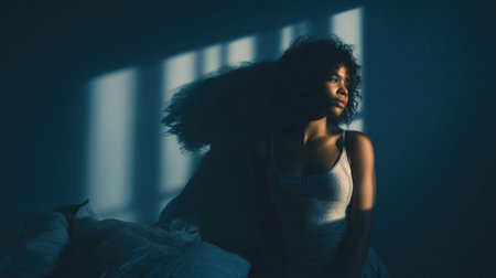 A solitary woman sits quietly in a dimly lit room, soft sunlight filtering through windows, highlighting her thoughtful expression and casting dramatic shadows.の素材
