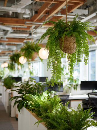 Modern office space featuring lush hanging ferns and desk plants creating a tranquil atmosphere, with natural light filtering through large windows.の素材