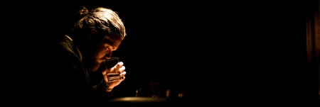 A man sits quietly in a dark bar, holding a glass of whiskey close to his face, lost in thought during a quiet evening.の素材