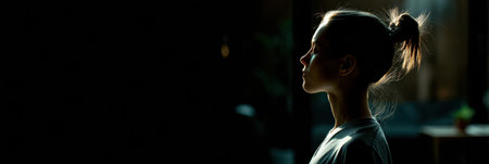 A girl stands quietly in a softly illuminated space, her silhouette striking against a dark background, reflecting a moment of peace and introspection.の素材