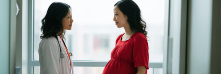 A doctor and a pregnant woman have a conversation in a bright, modern medical office, focusing on prenatal health and care.の素材