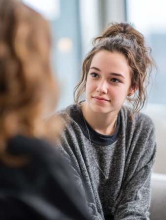 A young woman sits in a cozy space, listening attentively while conversing with a friend. Natural light brightens the contemporary interior around them.の素材