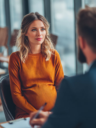 A pregnant woman wearing an orange dress sits in a contemporary office setting, engaged in a discussion with a man in a suit, showcasing a warm exchange.の素材