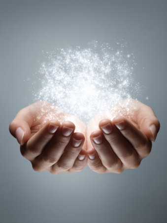 Two hands gently cradle a dazzling cloud of sparkling particles, creating a mesmerizing display of light and energy against a soft gray background.の素材