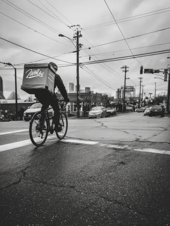 A cyclist rides through a city intersection, delivering goods in a weathered neighborhood on a cloudy afternoon, showcasing urban life in motion.の素材