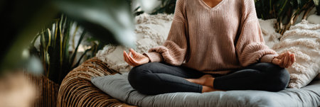 A woman sits cross-legged on a soft surface, practicing meditation in a tranquil indoor environment filled with greenery, promoting calmness and focus.の素材