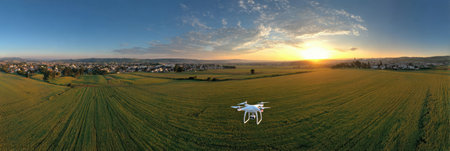 A drone hovers above a vast green field during sunset, capturing the natural beauty of the landscape and the colorful sky in the evening light.の素材