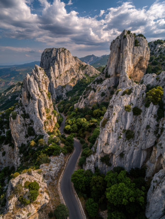 Scenic view of rugged mountains and a serene road meandering through lush greenery during the day, capturing the beauty of nature.の素材