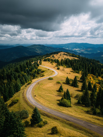 A winding road means through green hills, leading to distant mountains under a cloudy sky, showing the tranquility of the natural landscape.の素材
