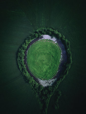 Aerial view of a vibrant circular field enclosed by lush trees. The scene showcases early morning light, highlighting the green grass and serene atmosphere.の素材