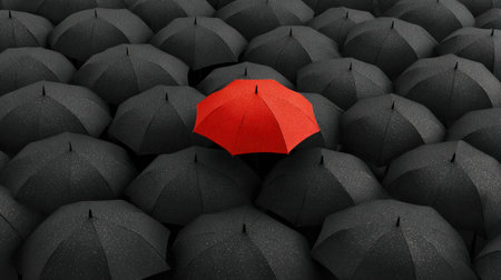 A vibrant red umbrella is surrounded by many black umbrellas, creating a striking contrast in a rainy urban environment.の素材