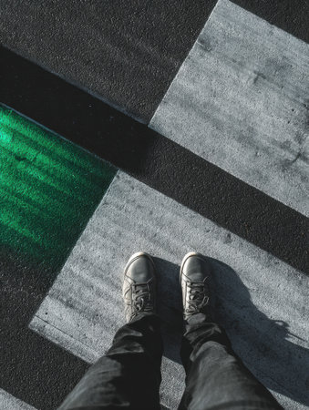 A person with gray shoes is standing on a striking black and white striped pavement, accentuated by a splash of green light.の素材