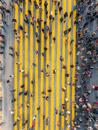 Many people walk across yellow pedestrian lanes on a bustling street under bright sunlight, showing urban life and activity.の素材