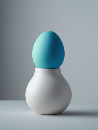 A smooth white ceramic base holds a vibrant blue egg in a minimalist space, showing simple lines and calming colors under soft lighting.の素材