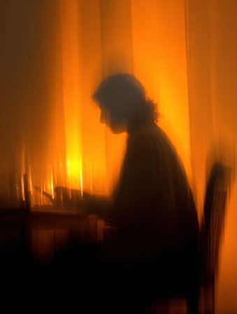 A quiet scene captures a persons silhouette sitting at a table, deeply engaged in their work, surrounded by warm, glowing light in the background.の素材
