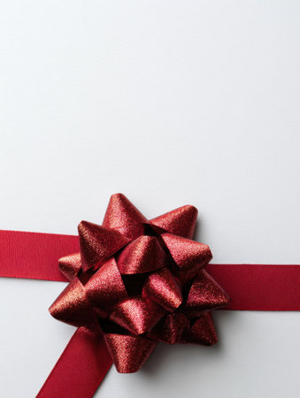A vibrant red gift bow is placed on a smooth white surface, evoking feelings of joy and anticipation associated with celebrations and gift-giving.の素材