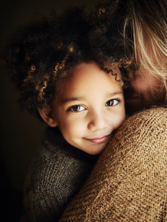 A child with curly hair enjoys a tender hug with a caregiver, showing happiness and affection in a cozy, intimate setting.の素材
