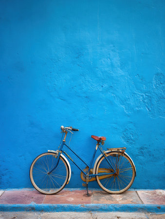 A vintage bicycle stands against a striking blue wall, adding character to the urban scene during daylight. The simple setting evokes a sense of nostalgia.の素材