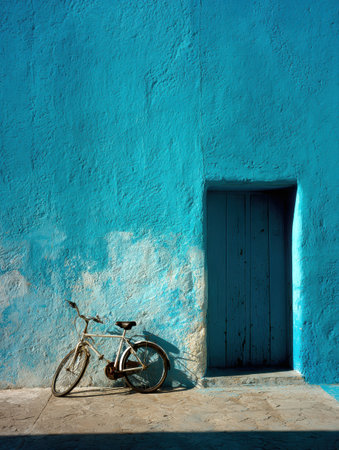 A charming white bicycle leans against a vibrant blue wall next to a wooden door, highlighting the beauty of everyday life in a colorful setting.の素材
