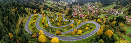Colorful trees frame a curvy road in a mountainous area, showing vibrant autumn colors and charming houses in the distance.の素材