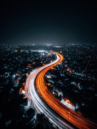 View of a vibrant urban landscape at night with a winding road illuminated by long light trails from moving vehicles and a distant skyline.の素材