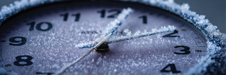 Clock face is adorned with intricate frost, showing delicate ice crystals on numbers and hands, emphasizing the chill of the winter season.の素材