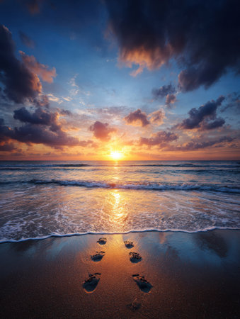 Footprints in the sand lead towards the waves as a vibrant sunset paints the sky in shades of orange and purple, creating a serene beach scene.の素材