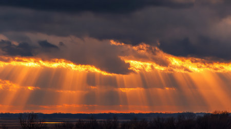 Golden rays of sunlight pierce through dark clouds during a stunning sunset, creating a dramatic panorama over the tranquil landscape at dusk.の素材