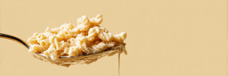 Curly pasta on a silver spoon in creamy sauce, a cozy comfort food moment against a soft beige backdrop.の素材