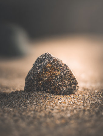 A textured rock sits prominently on a sandy surface, bathed in soft light, showing its natural colors and details.の素材