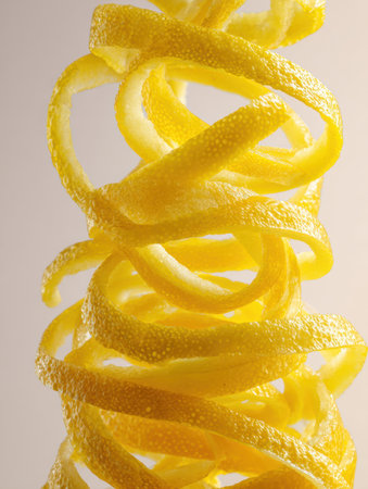 Yellow lemon peels spiral against a light background, showing their texture and vibrant color in an artistic display.の素材