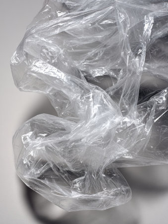Crumpled plastic wrap on a flat surface catches light, creating soft shadows and reflections that show its texture.の素材
