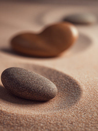 Smooth stones rest in fine sand, forming tranquil patterns and a heart shape, creating a serene and calming atmosphere.の素材