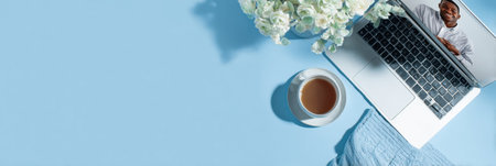 A cozy workspace with a laptop showing a smiling person on a video call, plus a warm drink and flowers.の素材