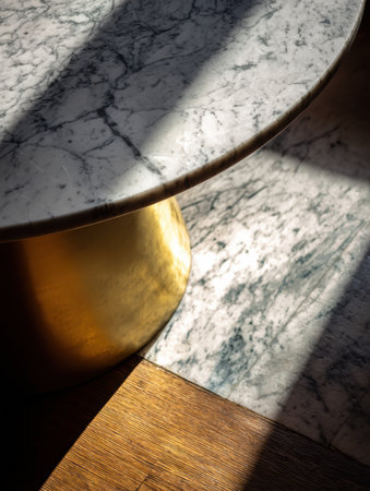 Sunlight illuminates a marble table with a golden base, casting striking shadows on the wooden floor in a stylish room.の素材