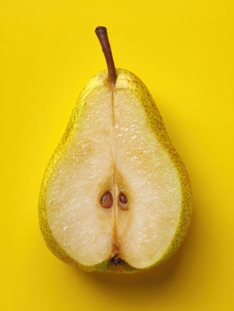 A bright yellow backdrop highlights a halved pear, showing its smooth flesh and fresh seeds.の素材