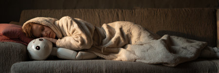 A child is sleeping soundly on a couch, holding a plush toy while wrapped in a plush blanket in a tranquil environment.の素材